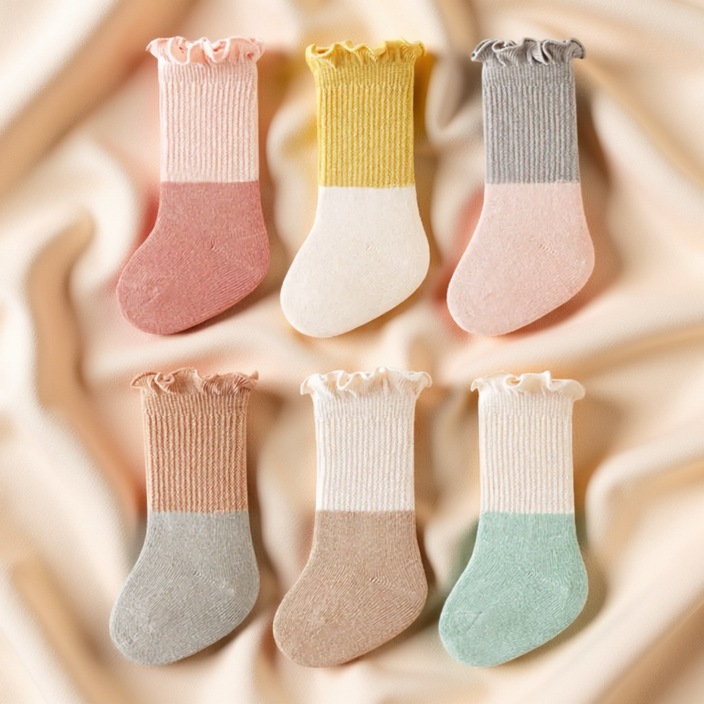 A collection of six colorful baby socks arranged in a grid pattern on a beige fabric background.